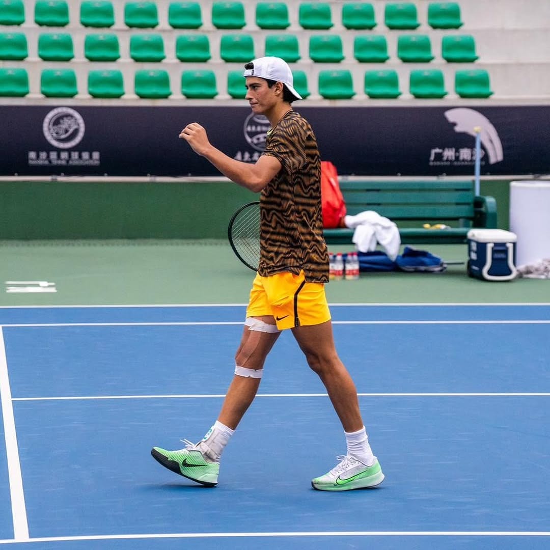 Federico pumps his fist while walking on a blue hardcourt, racket in hand, green empty stands and Chinese signage behind him.