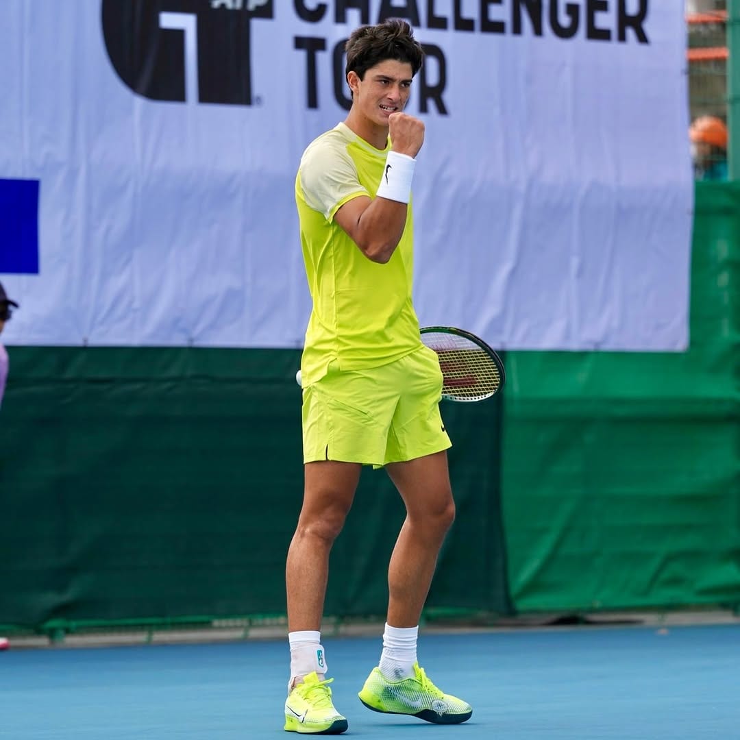 Federico Cinà pumps his fist in celebration on a hard court, racket in hand, ATP Challenger Tour banner behind him.