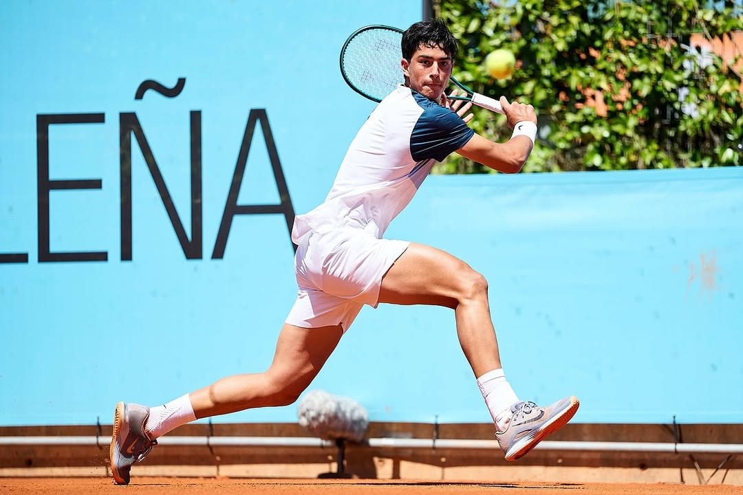 Federico Cinà stretches into a running backhand on red clay, mid-stride, with a light blue Mutua Madrid Open hoarding behind him.