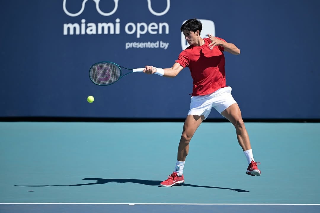 Federico Cinà hits a forehand on the blue hard court, mid-stride, Miami Open signage visible behind him.