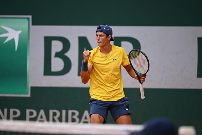 Federico Cinà pumps his fist in celebration on clay, holding a Wilson racket, BNP Paribas signage visible behind him.